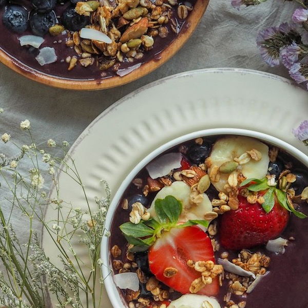 The Rainbow açaí bowl with strawberry, banana, blueberry and granola, styled with botanicals