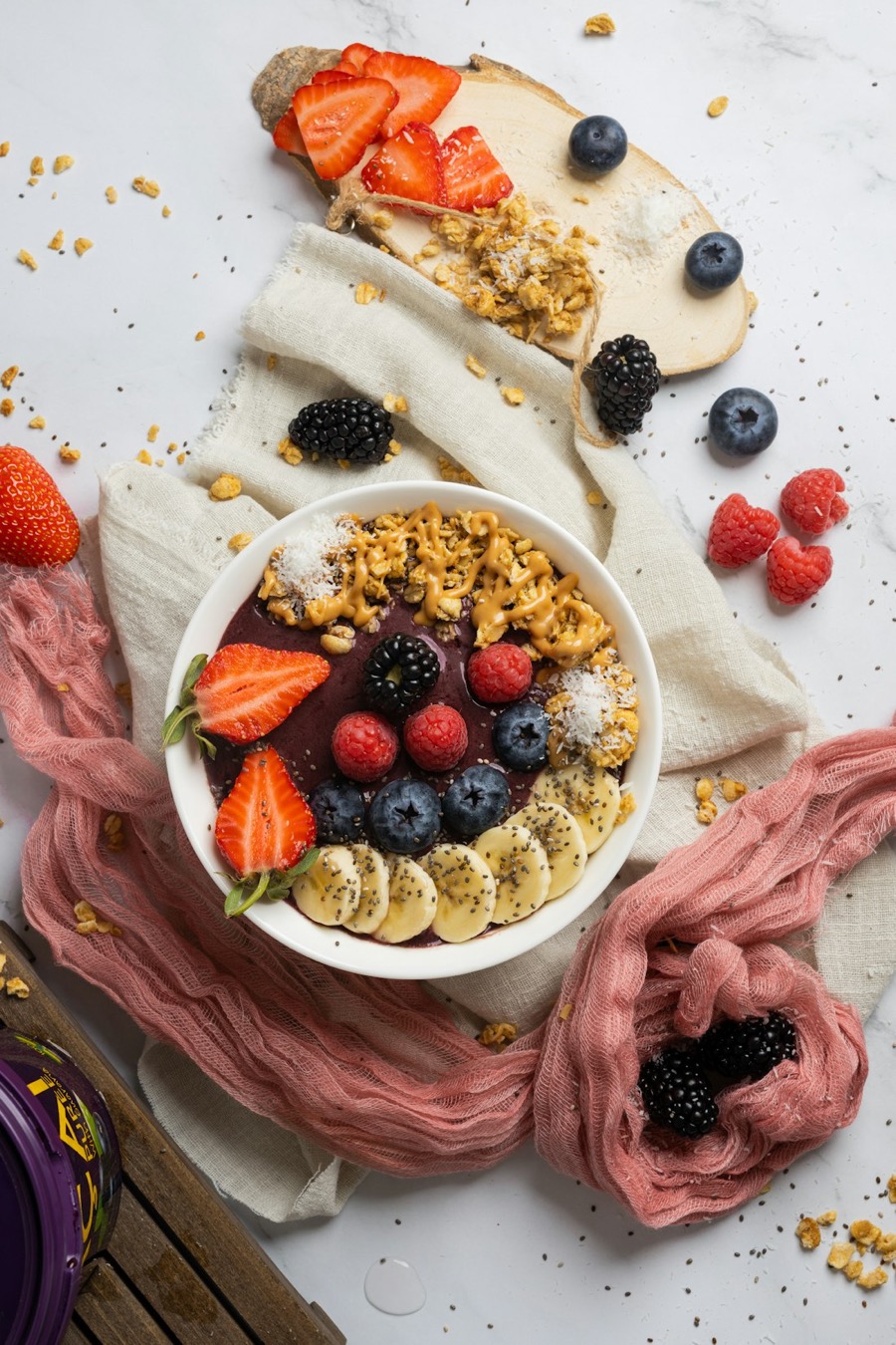 An açaí bowl with strawberry, banana, berries and granola, styled on soft linen